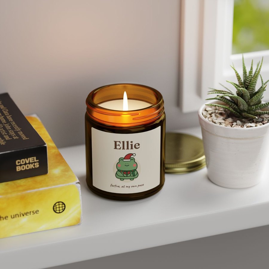 Lit candle in an amber jar on a windowsill, labelled Ellie with the Christmas frog