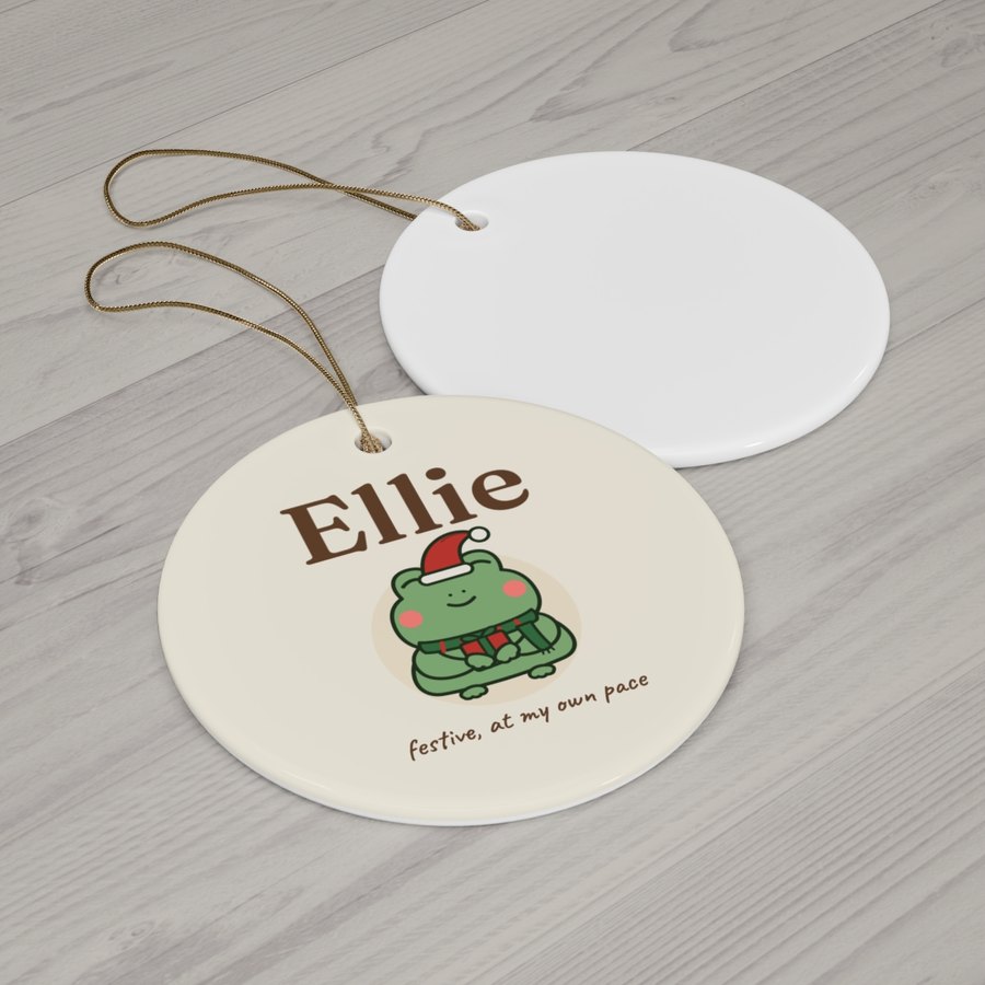 Round ceramic ornament with a gold string, printed Ellie above the Christmas frog